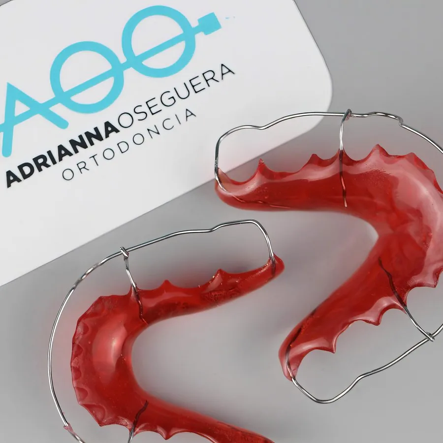 Two removable Hawley retainers with red acrylic and metal wire next to an AOO Ortodoncia card